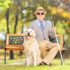Senior blind gentleman sitting on a bench with his dog, in a par
