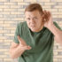 Young man with hearing problem on brick wall background