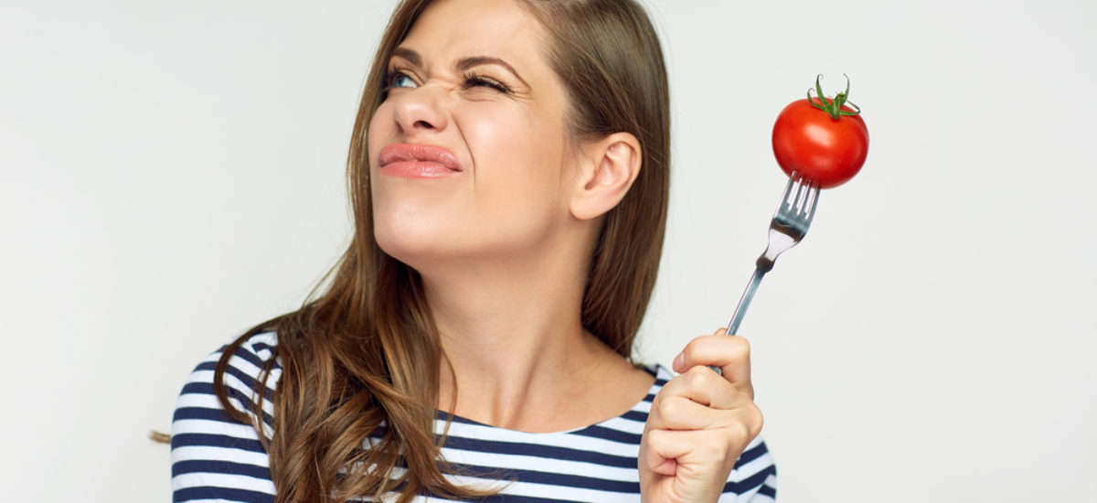 Woman holding tomato on fork looking up.
