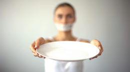 Skinny woman with taped mouth showing empty plate, concept of fasting, hunger